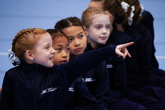 Young gymnasts in Casey Gymnastics uniforms watching a competition together